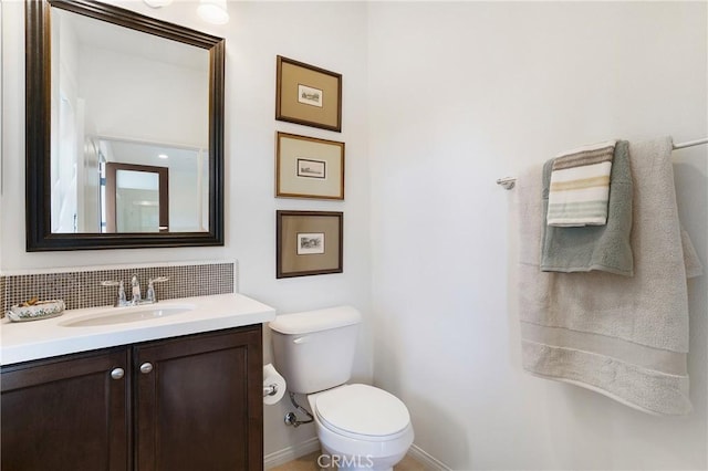 bathroom featuring backsplash, toilet, baseboards, and vanity