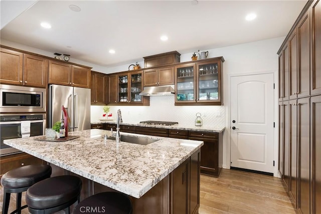 kitchen with light wood-style floors, a kitchen bar, light stone counters, a sink, and appliances with stainless steel finishes