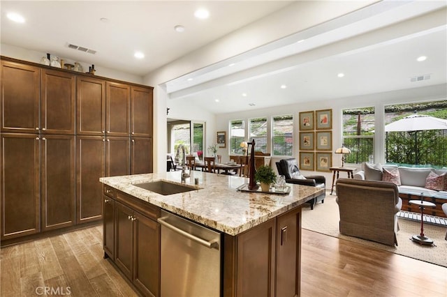 kitchen featuring stainless steel dishwasher, a sink, light stone counters, open floor plan, and light wood-style floors