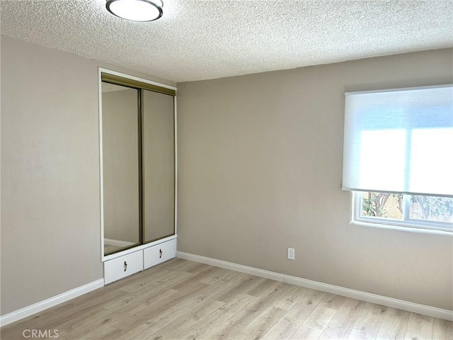 unfurnished room with a textured ceiling, baseboards, and light wood-style flooring