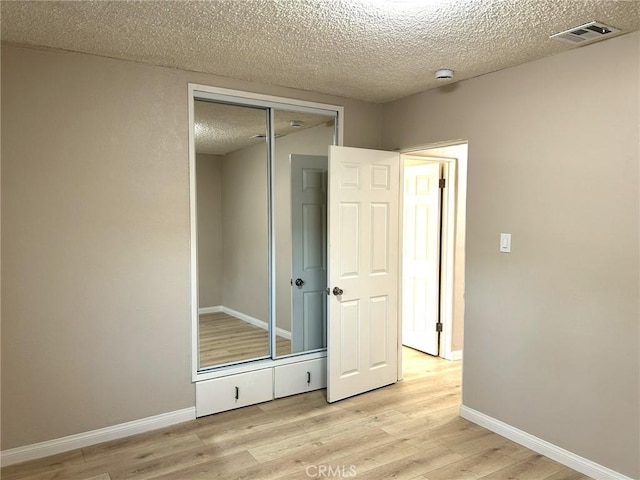 unfurnished bedroom with visible vents, a textured ceiling, light wood-style floors, and baseboards