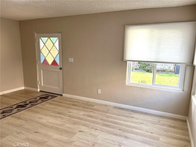 foyer entrance featuring a textured ceiling, baseboards, and light wood-style floors