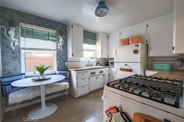 kitchen with a sink, light tile patterned floors, white cabinets, and white appliances