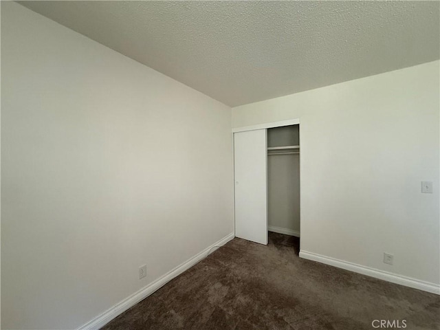 unfurnished bedroom with dark carpet, a textured ceiling, baseboards, and a closet