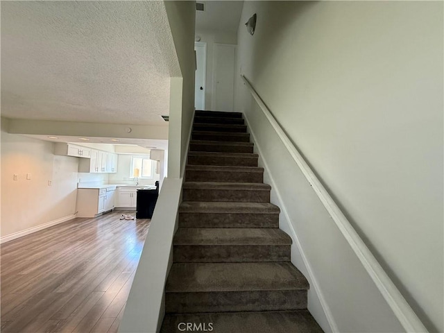 stairs with baseboards, a textured ceiling, and wood finished floors