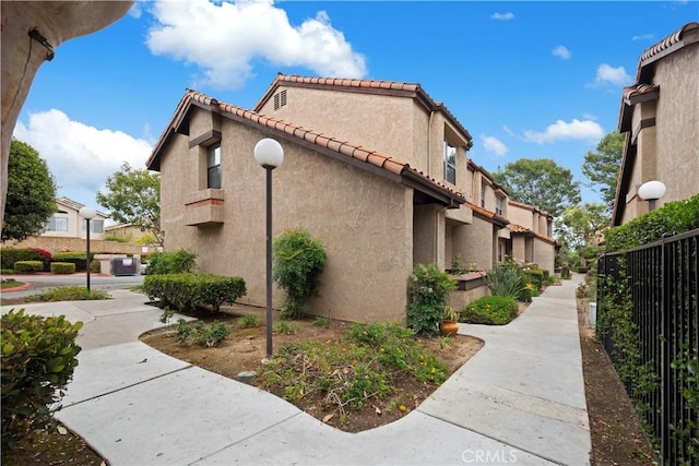 view of side of property with fence, stucco siding, a tile roof, and a residential view
