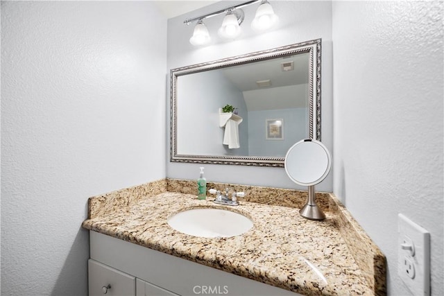bathroom with a textured wall, visible vents, and vanity