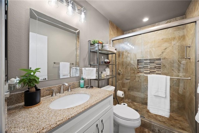 full bathroom featuring vanity, a textured wall, a shower stall, and toilet