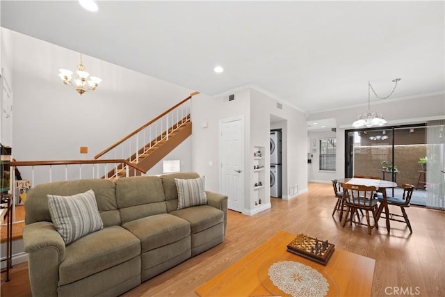 living area featuring stacked washer / drying machine, an inviting chandelier, visible vents, and light wood-style floors