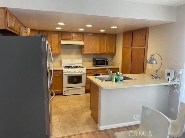 kitchen with brown cabinets, a peninsula, appliances with stainless steel finishes, and under cabinet range hood