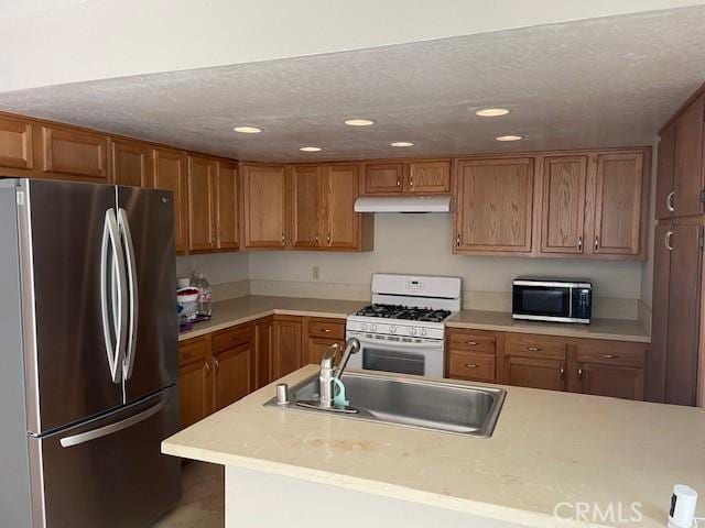 kitchen with a sink, light countertops, brown cabinetry, stainless steel appliances, and under cabinet range hood
