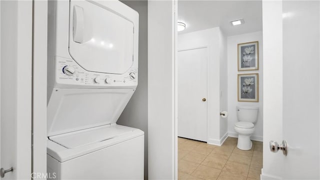 clothes washing area with baseboards, light tile patterned floors, laundry area, and stacked washer / dryer