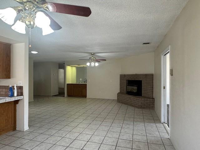 unfurnished living room with ceiling fan, a fireplace, a textured ceiling, light tile patterned floors, and visible vents
