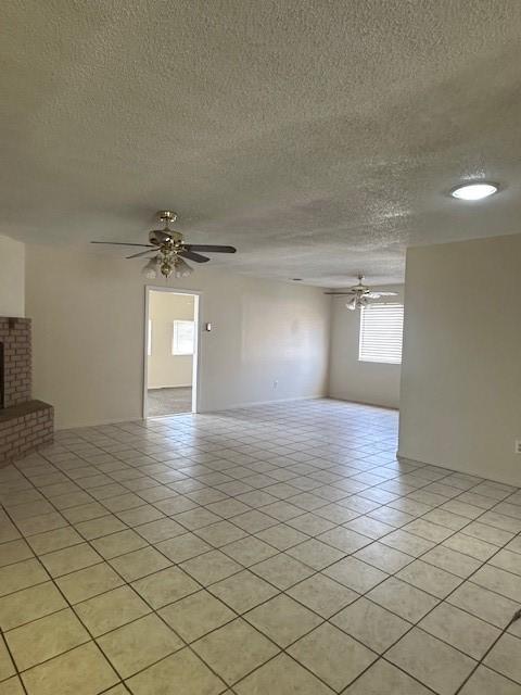 unfurnished room with a ceiling fan, a textured ceiling, light tile patterned flooring, and a fireplace