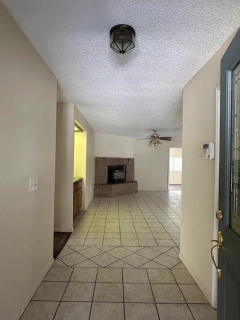 unfurnished living room featuring light tile patterned floors, a ceiling fan, a textured ceiling, and a brick fireplace
