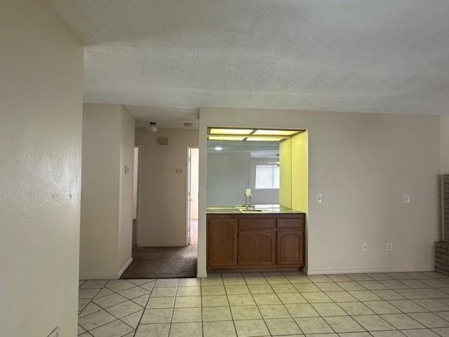 unfurnished room with baseboards, a sink, a textured ceiling, and light tile patterned floors