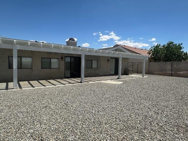 rear view of property featuring a chimney, a patio area, fence, a pergola, and stucco siding