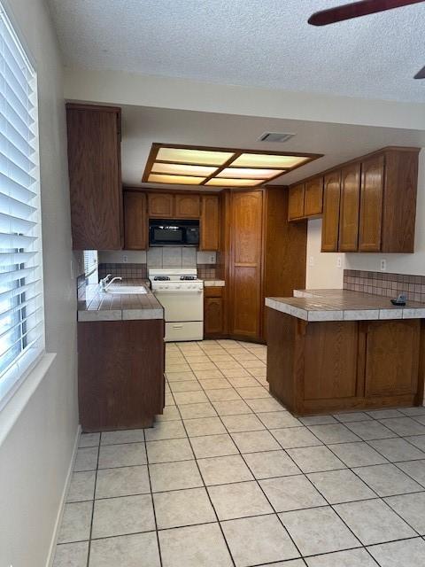 kitchen with a peninsula, black microwave, white range with gas stovetop, brown cabinets, and light tile patterned floors