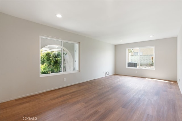 spare room with baseboards, recessed lighting, wood finished floors, and a wealth of natural light