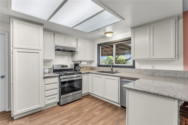 kitchen featuring a sink, stainless steel appliances, a peninsula, light wood-type flooring, and under cabinet range hood