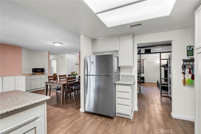 kitchen featuring freestanding refrigerator, white cabinets, visible vents, and light wood finished floors