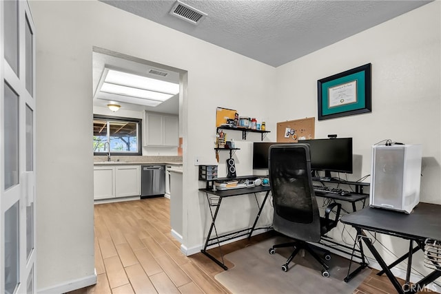 home office featuring light wood-type flooring, a sink, a textured ceiling, and visible vents