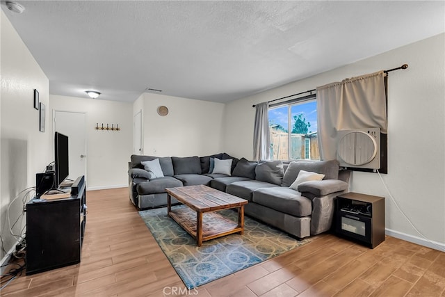 living room with visible vents, a textured ceiling, light wood-style flooring, and baseboards