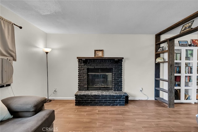 living area featuring a textured ceiling, baseboards, a fireplace, and wood finished floors