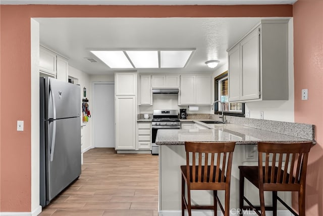 kitchen featuring a peninsula, baseboards, light stone counters, a sink, and appliances with stainless steel finishes