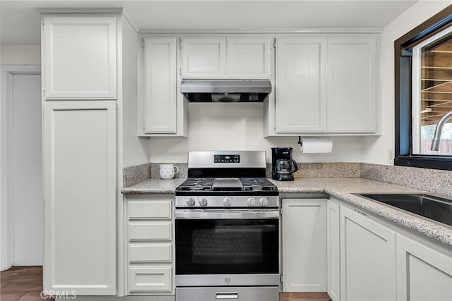 kitchen featuring light stone counters, ventilation hood, white cabinets, stainless steel range with gas stovetop, and a sink
