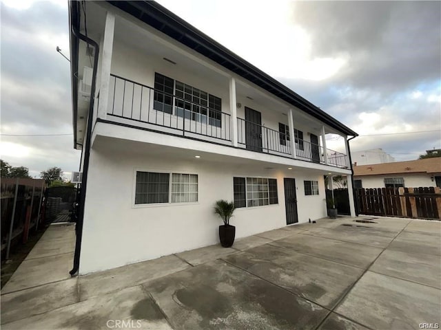 rear view of house featuring fence, stucco siding, and a balcony