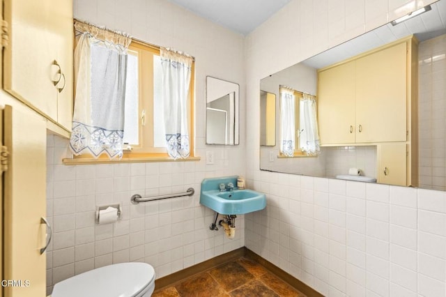 bathroom with toilet, a sink, tile walls, and a wealth of natural light