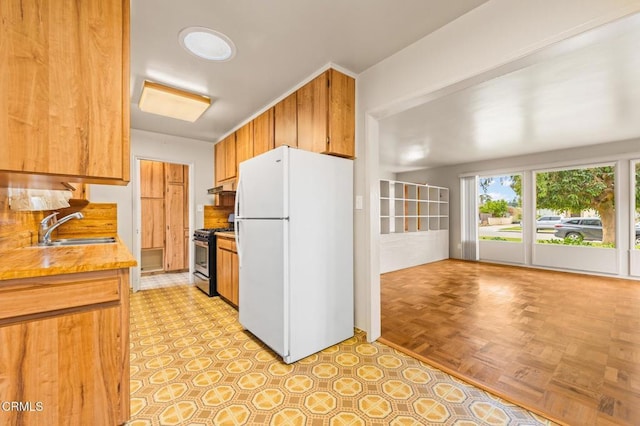kitchen with freestanding refrigerator, light countertops, under cabinet range hood, a sink, and gas stove