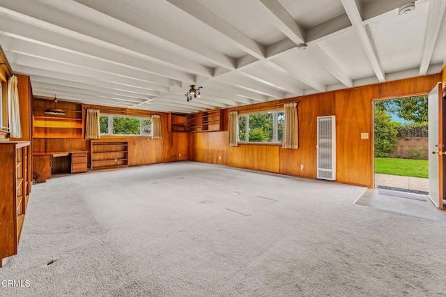 unfurnished living room featuring wooden walls, plenty of natural light, beamed ceiling, and a heating unit