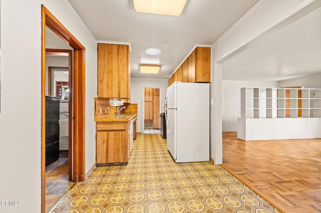 kitchen featuring freestanding refrigerator, brown cabinets, a sink, and light countertops