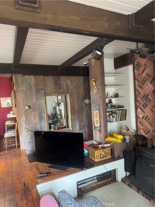 living area with beamed ceiling, wood walls, a wood stove, and hardwood / wood-style floors