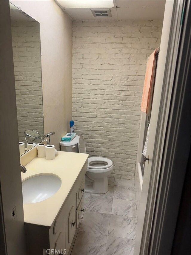 full bath featuring brick wall, walk in shower, vanity, toilet, and marble finish floor