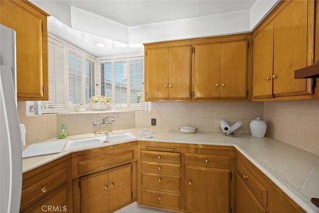 kitchen featuring a sink, decorative backsplash, brown cabinetry, and tile countertops
