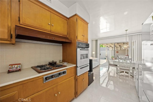 kitchen featuring brown cabinets, white oven, a warming drawer, under cabinet range hood, and light tile patterned flooring