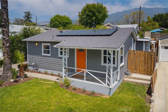 view of front of house with solar panels, roof with shingles, and a front lawn