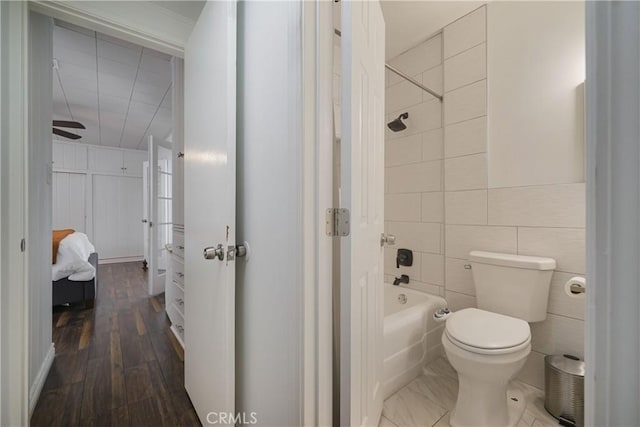 bathroom featuring wood finished floors, toilet, tile walls, shower / bath combination, and a ceiling fan