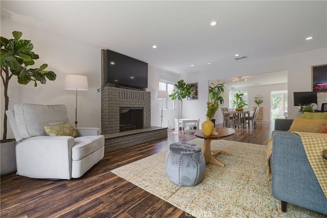 living room with a brick fireplace, recessed lighting, and dark wood-type flooring