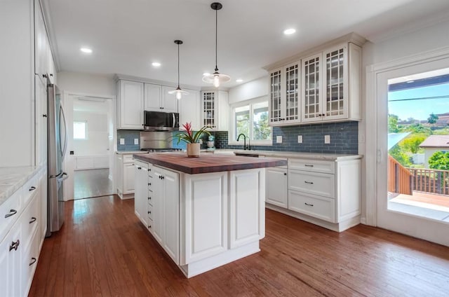 kitchen with wooden counters, dark wood-style flooring, backsplash, appliances with stainless steel finishes, and a center island