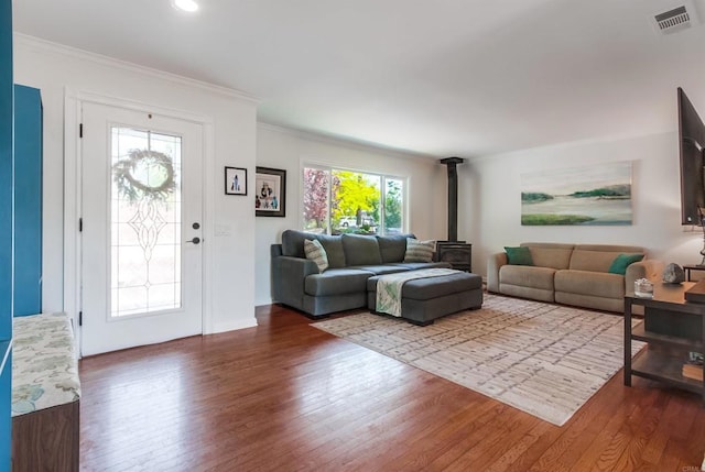 living area with visible vents, a wood stove, wood finished floors, and ornamental molding