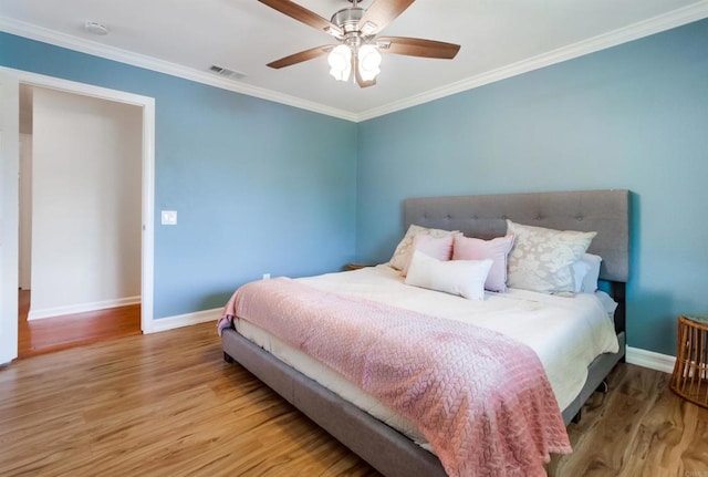 bedroom with visible vents, ornamental molding, wood finished floors, baseboards, and ceiling fan