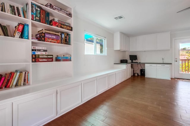 kitchen with white cabinets, visible vents, built in desk, and wood finished floors