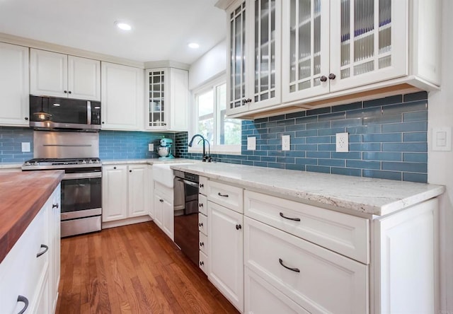 kitchen with wood finished floors, a sink, butcher block counters, glass insert cabinets, and stainless steel appliances