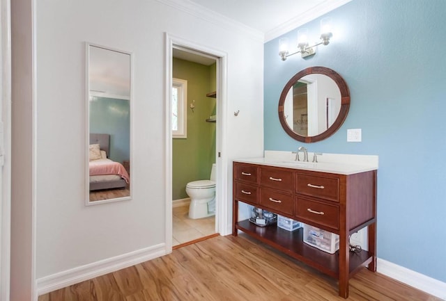 ensuite bathroom with crown molding, wood finished floors, toilet, and vanity