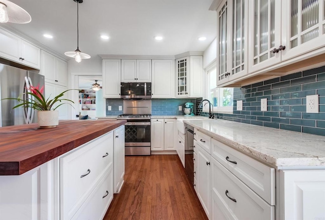 kitchen with butcher block counters, ceiling fan, dark wood-style floors, a sink, and stainless steel appliances