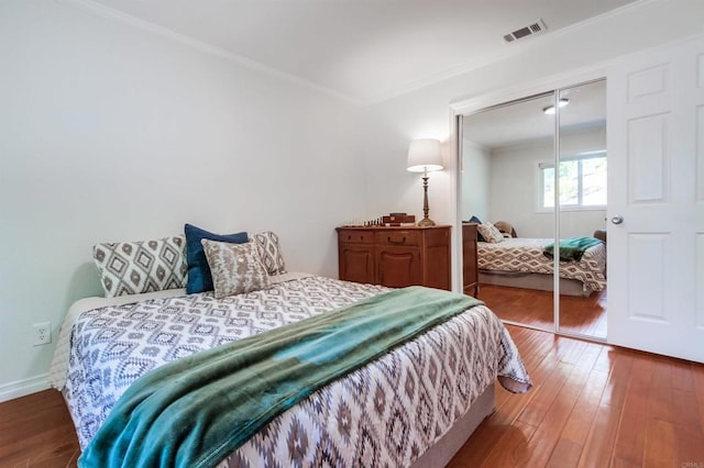 bedroom with crown molding, baseboards, wood finished floors, visible vents, and a closet